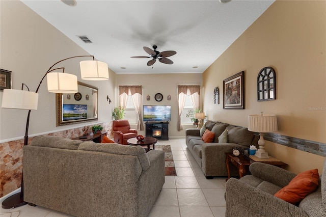 living room with visible vents, ceiling fan, a lit fireplace, and light tile patterned floors