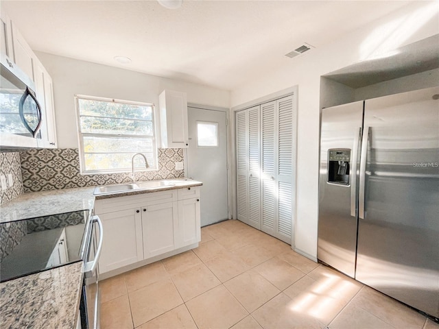 kitchen with stainless steel appliances, visible vents, decorative backsplash, white cabinetry, and a sink