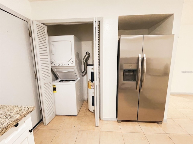 laundry area featuring stacked washer and clothes dryer, light tile patterned floors, water heater, and laundry area