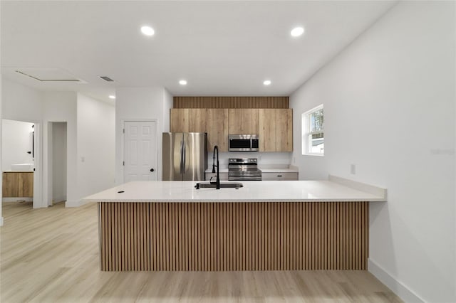 kitchen with light wood finished floors, a peninsula, a sink, light countertops, and appliances with stainless steel finishes