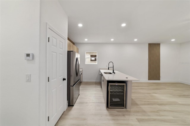 kitchen with beverage cooler, light wood finished floors, recessed lighting, freestanding refrigerator, and a sink