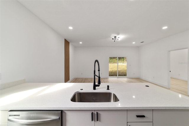 kitchen featuring open floor plan, light wood-type flooring, light stone counters, stainless steel dishwasher, and a sink