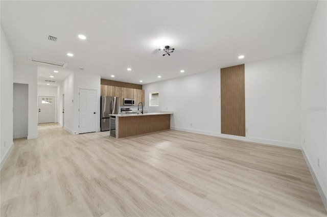 unfurnished living room with recessed lighting, baseboards, light wood finished floors, and a sink