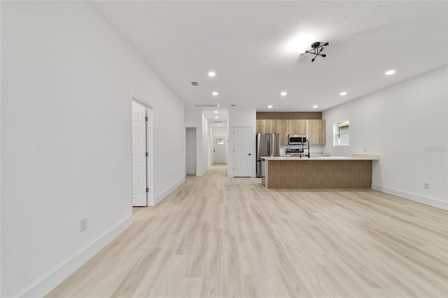 interior space featuring light countertops, appliances with stainless steel finishes, a peninsula, brown cabinetry, and modern cabinets