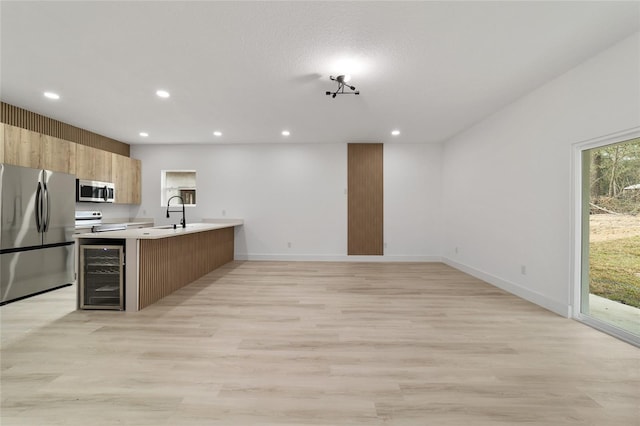 kitchen featuring beverage cooler, recessed lighting, a peninsula, appliances with stainless steel finishes, and light countertops