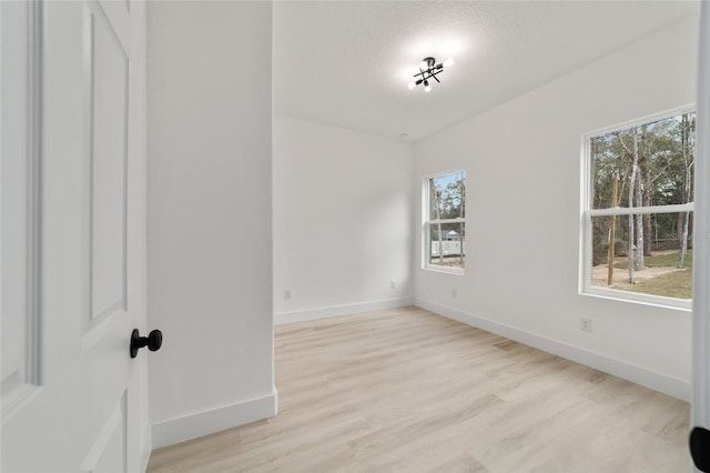 spare room featuring light wood-style floors, baseboards, and a textured ceiling