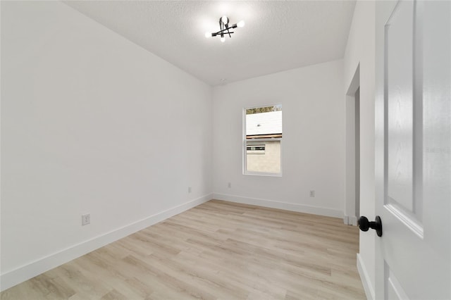 empty room with light wood-type flooring, baseboards, and a textured ceiling