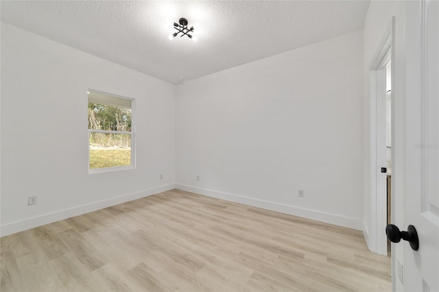 spare room with baseboards, light wood finished floors, and a textured ceiling