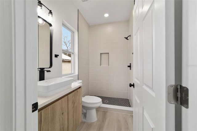 bathroom with toilet, tiled shower, vanity, and wood finished floors