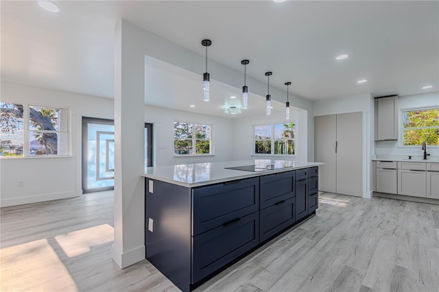 kitchen featuring black electric stovetop, gray cabinetry, a sink, light countertops, and decorative light fixtures