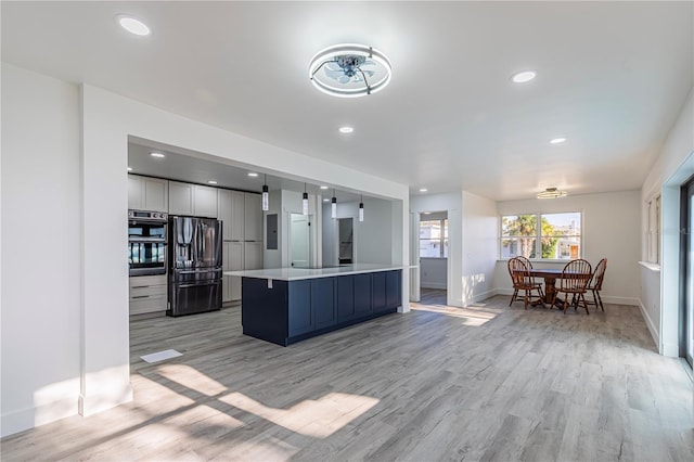 kitchen with double oven, light wood-style flooring, a kitchen island, refrigerator with ice dispenser, and light countertops