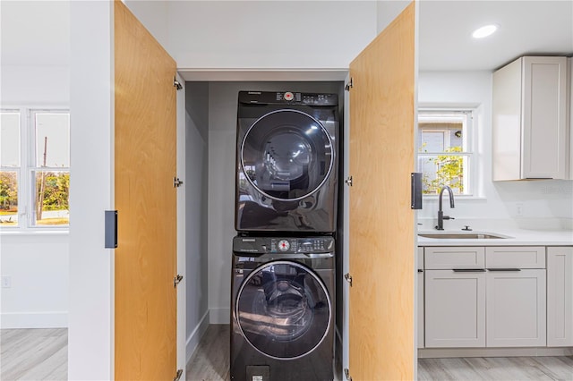 laundry room featuring laundry area, stacked washer / dryer, a sink, and baseboards