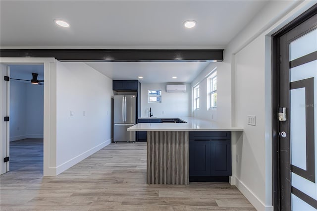 kitchen with a wall unit AC, a breakfast bar area, light countertops, freestanding refrigerator, and a peninsula