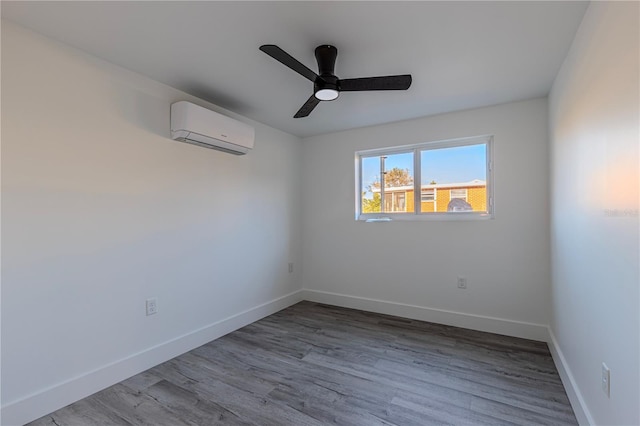 empty room featuring a wall mounted AC, wood finished floors, a ceiling fan, and baseboards