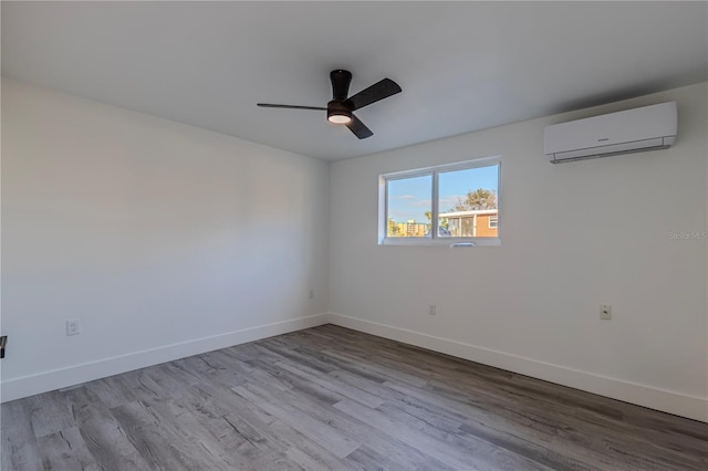 unfurnished room with a ceiling fan, light wood-type flooring, a wall unit AC, and baseboards