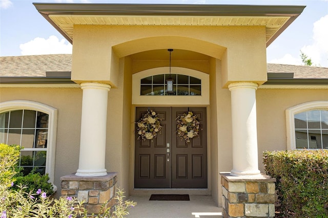 property entrance featuring covered porch, roof with shingles, and stucco siding