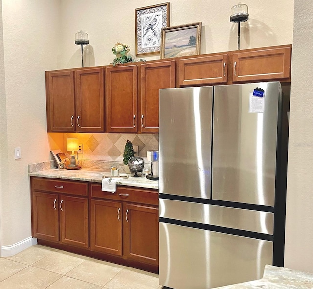 kitchen featuring brown cabinets, freestanding refrigerator, light tile patterned floors, decorative backsplash, and baseboards