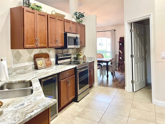 kitchen with beverage cooler, light stone counters, tasteful backsplash, stainless steel appliances, and light tile patterned floors