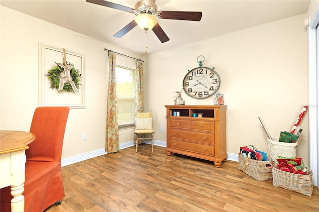 living area with a ceiling fan, baseboards, and light wood-type flooring