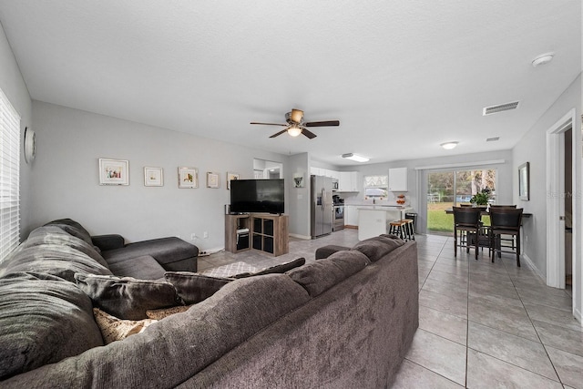 living room with light tile patterned floors, a textured ceiling, visible vents, baseboards, and a ceiling fan