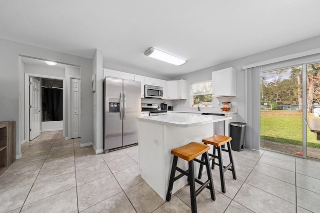 kitchen with white cabinets, appliances with stainless steel finishes, a kitchen breakfast bar, a center island, and light countertops