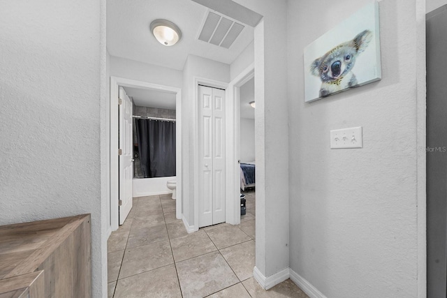 corridor featuring light tile patterned floors, baseboards, visible vents, and a textured wall