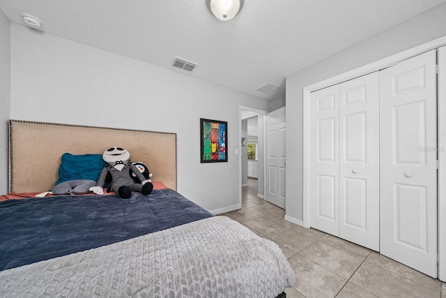 bedroom with a textured ceiling, light tile patterned flooring, visible vents, baseboards, and a closet