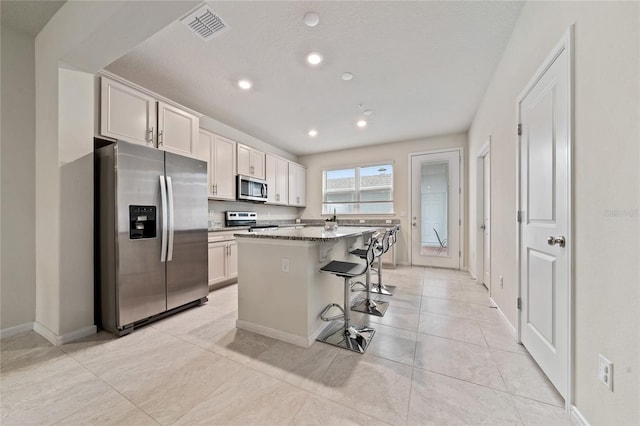 kitchen with white cabinets, a kitchen island, light stone counters, a kitchen breakfast bar, and stainless steel appliances