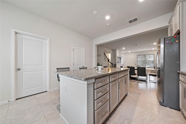 kitchen with visible vents, a kitchen island, open floor plan, freestanding refrigerator, and light stone countertops