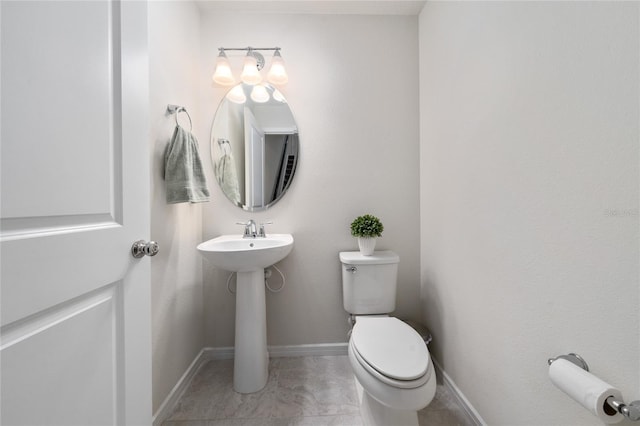 half bathroom featuring a sink, tile patterned floors, toilet, and baseboards