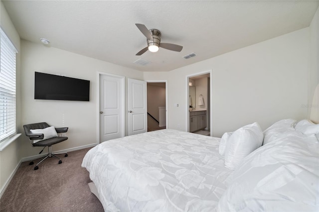 carpeted bedroom with a ceiling fan, visible vents, ensuite bath, and baseboards