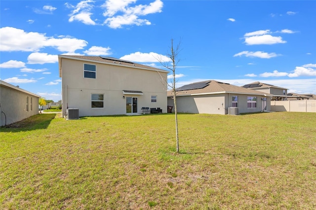 rear view of property with stucco siding, central AC, a lawn, and solar panels