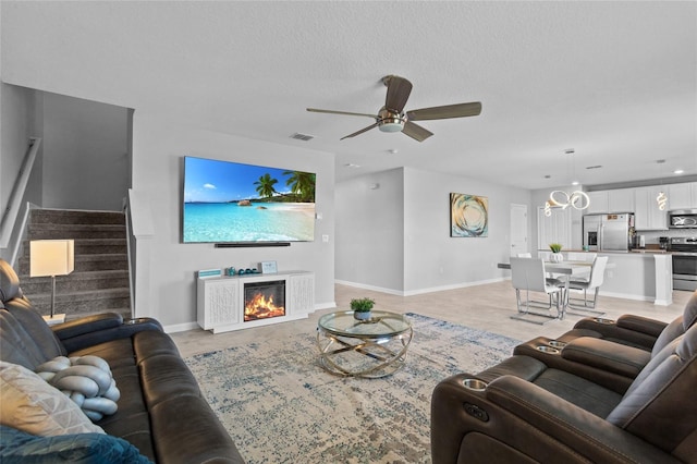 living room featuring visible vents, a ceiling fan, stairway, a lit fireplace, and a textured ceiling