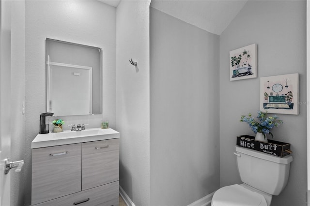 bathroom featuring lofted ceiling, baseboards, vanity, and toilet