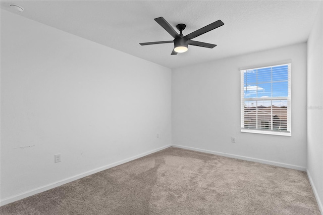 carpeted spare room with a ceiling fan and baseboards