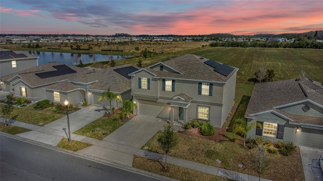 view of front of property with a garage, solar panels, a water view, driveway, and stucco siding