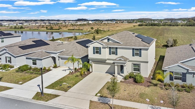 traditional home featuring driveway, a shingled roof, solar panels, a water view, and stucco siding