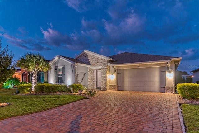 view of front facade with decorative driveway, stucco siding, an attached garage, stone siding, and a front lawn