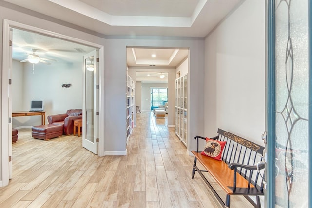 hallway featuring light wood-style floors, french doors, a raised ceiling, and baseboards