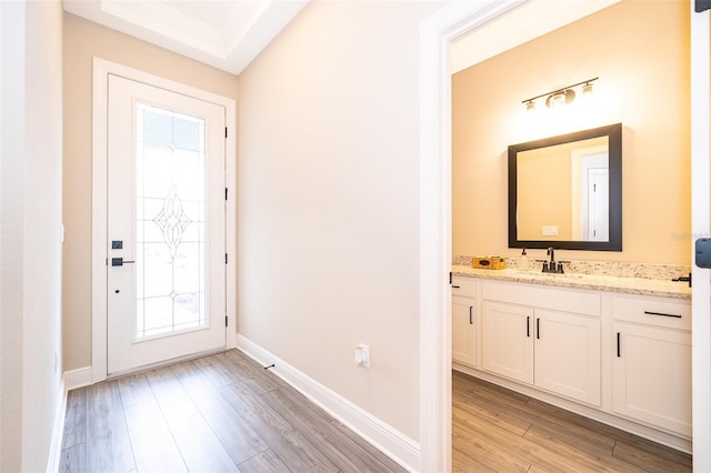 doorway featuring baseboards, a sink, and light wood finished floors