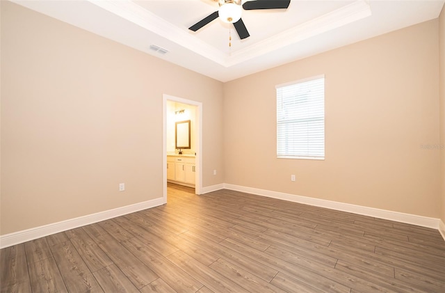 spare room with a raised ceiling, visible vents, a ceiling fan, wood finished floors, and baseboards