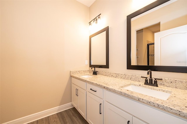 bathroom with double vanity, wood finished floors, a sink, and baseboards