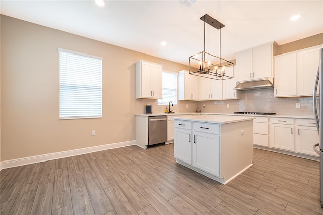 kitchen with tasteful backsplash, hanging light fixtures, stainless steel dishwasher, white cabinets, and under cabinet range hood