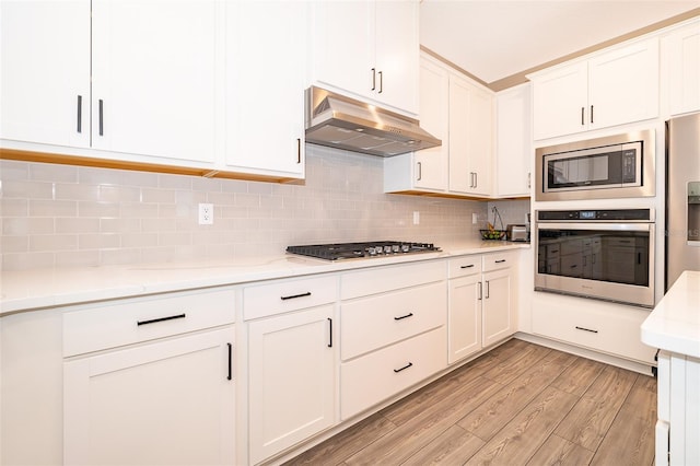 kitchen with light wood finished floors, backsplash, appliances with stainless steel finishes, white cabinets, and under cabinet range hood