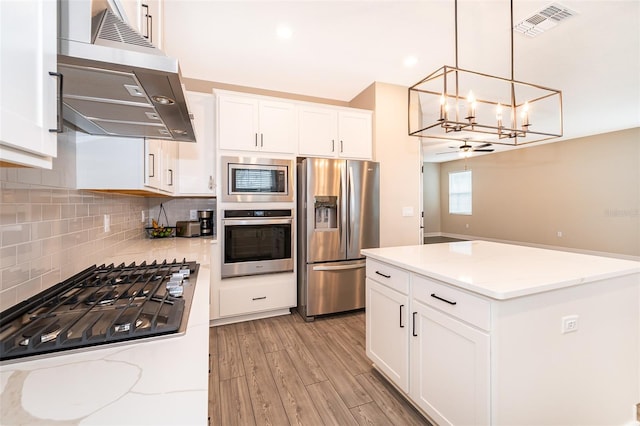 kitchen featuring stainless steel appliances, exhaust hood, white cabinets, light stone countertops, and pendant lighting