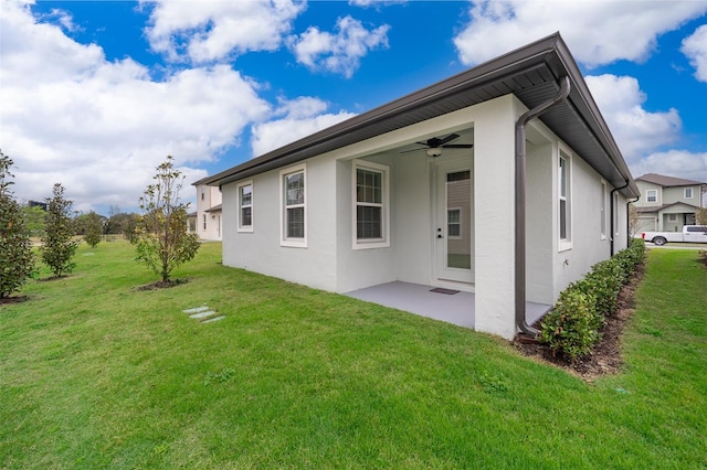 rear view of property featuring a patio area, a lawn, a ceiling fan, and stucco siding