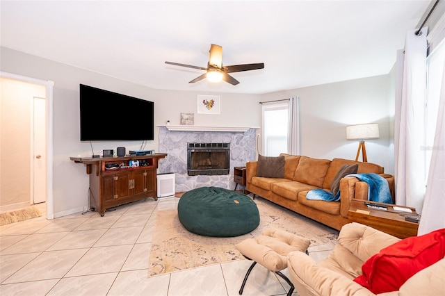 living room featuring a fireplace, baseboards, a ceiling fan, and light tile patterned flooring