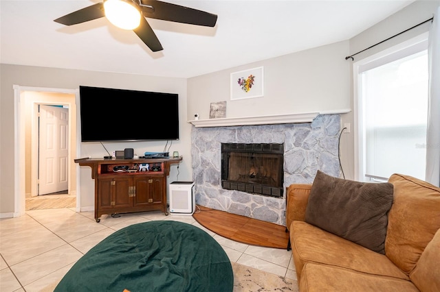 living area with ceiling fan, a fireplace, baseboards, and light tile patterned floors