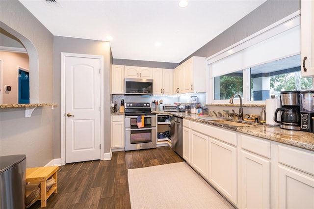 kitchen with light stone counters, dark wood-style flooring, stainless steel appliances, white cabinets, and a sink