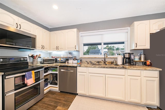 kitchen featuring white cabinets, wood tiled floor, stainless steel appliances, stone counters, and a sink